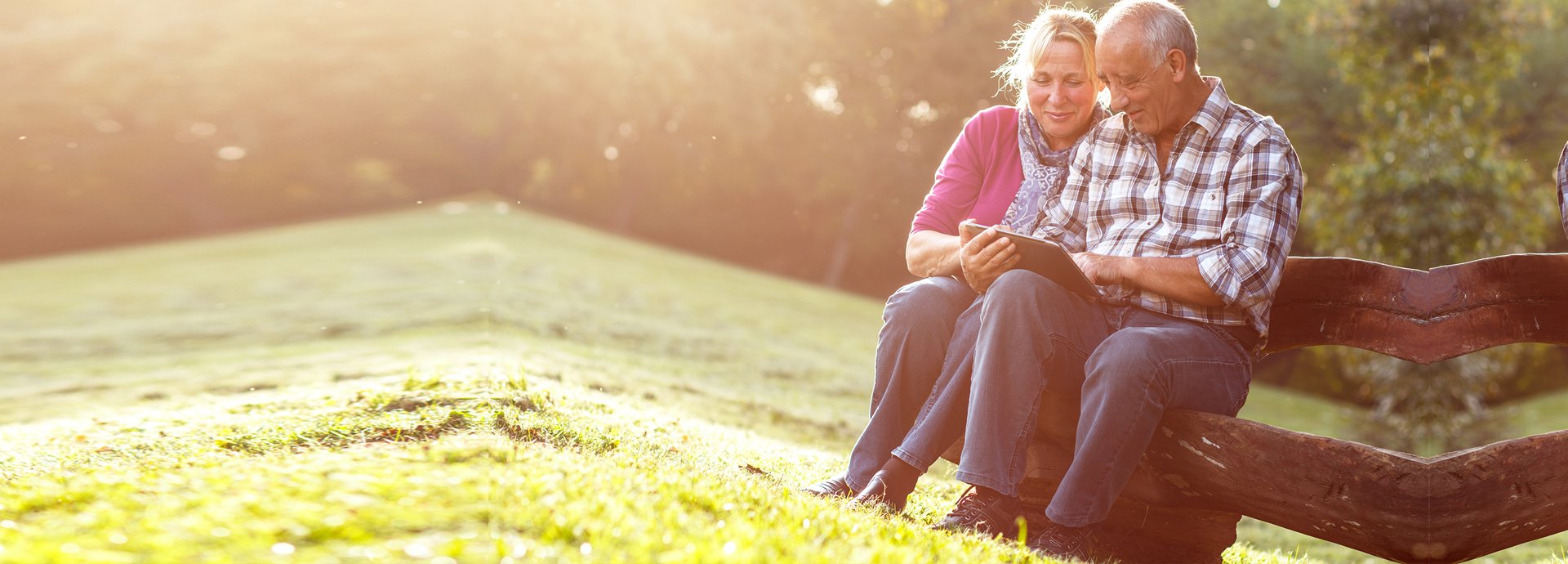 Older couple sitting on bench looking at tablet and laughing