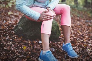 woman in winter exercise gear sits on rock, clutching knee 